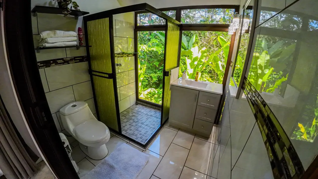 Baño con ducha de vidrio y vista abierta a jardín tropical en cabaña de La Fortuna